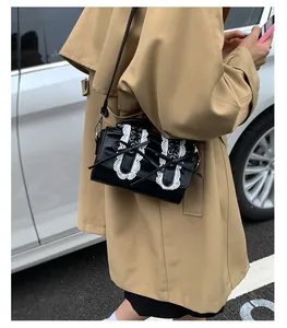 Bolso negro brillante con lazo y encaje llevado como bandolera sobre una gabardina