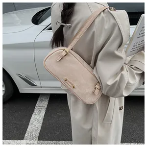 Primer plano de bolso bandolera beige mate con placa metálica sobre gabardina elegante