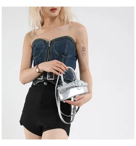Détail d'un sac argenté effet miroir porté avec un haut en jean bleu zippé stylé