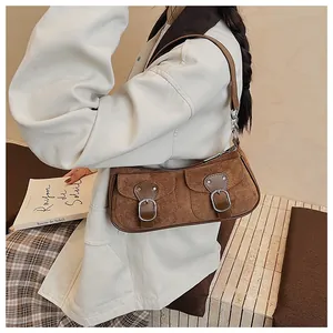 Detalle de bolso bandolera de ante marrón con bolsillos de hebilla y textura mate suave