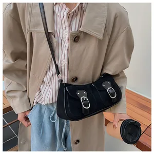Detalle de bolso retro de ante negro con hebillas plateadas llevado con una gabardina
