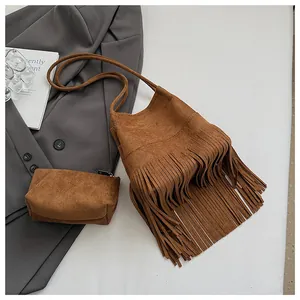 Detalle del bolso tipo cubo marrón con flecos y estuche sobre traje gris