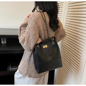 Detalle de un bolso cubo acolchado negro con cierre dorado y cadena en una modelo