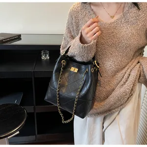 Detalle de bolso cubo de cuero acolchado negro con cadena dorada y cierre giratorio