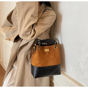 Detalle de bolso saco acolchado con patchwork de ante, cierre dorado y cadena mostrado en modelo
