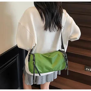 Detalle del bolso bandolera de nailon verde mostrando la forma cilíndrica y la cremallera
