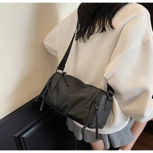 Bolso bandolera cilíndrico de nailon negro visto desde un lateral posterior en modelo