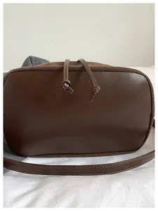 Detalle del bolso tipo cubo de ante marrón oscuro con cordón de cuero y nudo