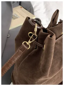 Detalle de hebillas doradas y textura de gamuza en el bolso tipo cubo marrón