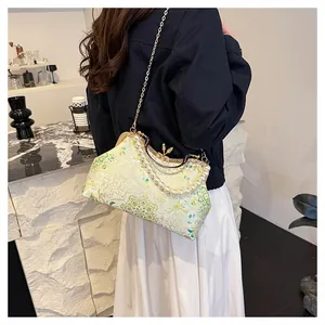 Detail of floral brocade shell bag with pearl handle and golden chain on a model