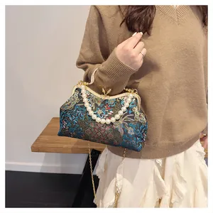 Detail of embroidered floral shell bag with elegant pearl handle and golden chain strap