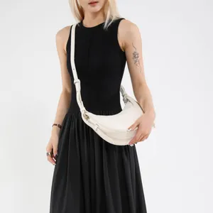 Sac hobo croissant en cuir blanc avec bandoulière réglable porté par un mannequin en noir
