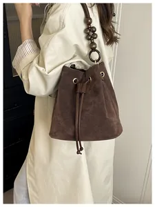Detalle de bolso bucket de ante marrón oscuro con correa de cuentas de madera y cordón ajustable