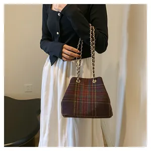 Detail of wool fabric plaid bucket bag with gold chain strap worn by a model