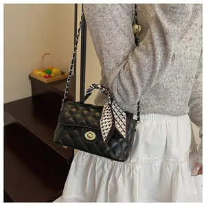 Détail d'un sac à main noir matelassé avec poignée en foulard de soie et chaîne dorée