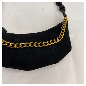 Detalle de bolso medialuna de ante negro con cadena dorada y correa con nudo decorativo