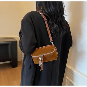 Détail d'un sac bandoulière en daim marron avec breloque robot sur un modèle en costume noir