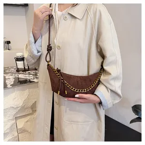 Bolso media luna de ante marrón con cadena dorada lucido por modelo con gabardina