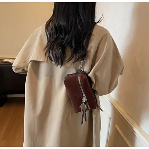 Détail du sac ceinture en daim marron avec breloque robot et franges sur manteau kaki