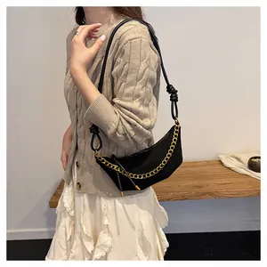 Detalle de bolso medialuna negro con cadena dorada y correa de nudo en modelo