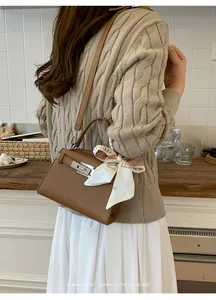 Detalle del bolso de cuero marrón con grano de lichi y pañuelo de seda en el asa superior