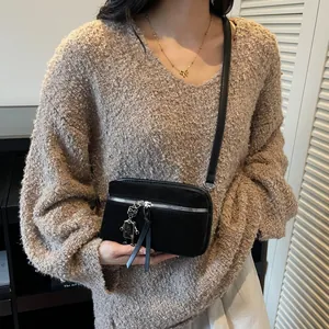 Sac bandoulière noir mat avec charm robot argenté sur pull beige en maille