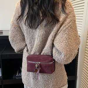 Sac bandoulière bordeaux en daim mat avec breloque en métal sur un pull en maille