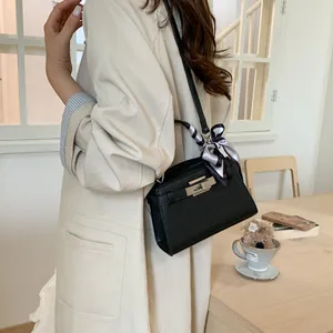 Bolso elegante negro con grabado de lichi y pañuelo de seda llevado por una modelo