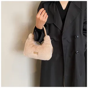 Détail d'un sac à main beige en peluche avec plaque métallique sur manteau noir