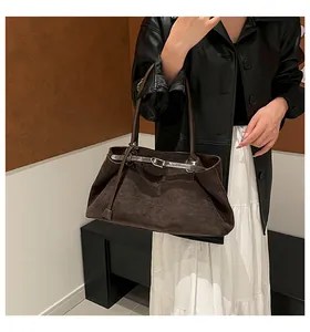 Detalle de un bolso tote de ante marrón oscuro con correas finas y hebillas metálicas