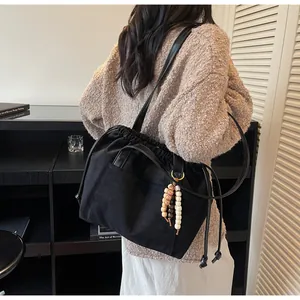 Detalle de bolso negro con cordón, colgante de cuentas de madera y bolsillo delantero