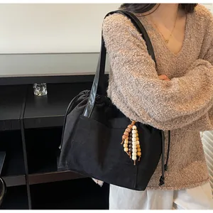 Detalle de bolso tote de ante negro con cierre de cordón y colgante de cuentas de madera