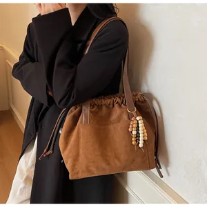 Detalle del bolso tote de ante sintético marrón con pliegues y colgante de borla con cuentas