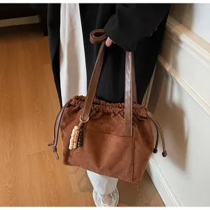 Detalle del bolso tote de ante marrón con cordón de ajuste y colgante de cuentas de madera