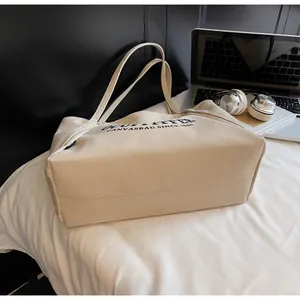 Detalle del bolso tote de lona blanco roto con letras Outfitter en un entorno de estilo de vida