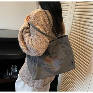 Primer plano de un bolso tote grande de lona gris con logo retro usado por una modelo