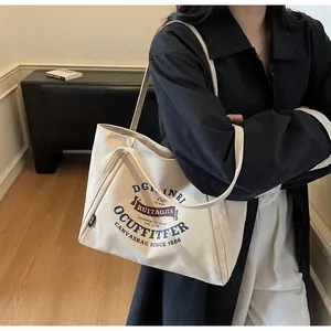 Detalle del bolso tote de lona beige con letras retro y correas largas para el hombro