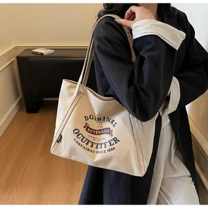 Detalle del bolso tote de lona beige con estampado retro sobre abrigo oscuro