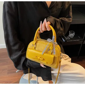 Detalle de bolso amarillo con lazo, ante combinado y cinta de cuadros en el asa