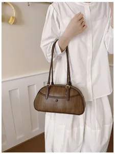 Détail d'un sac à bandoulière marron foncé avec texture tissée et fermoir rond décoratif