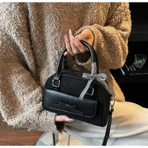 Detalle de bolso de ante negro con lazo de cinta a cuadros y detalles de cuero