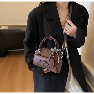 Detalle de bolso Boston de ante marrón con lazo de cuero y cinta de seda a cuadros