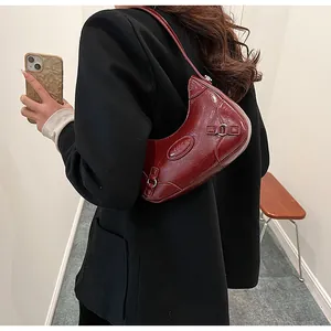 Detalle del bolso medialuna rojo vino en piel brillante con logotipo en relieve y hebilla