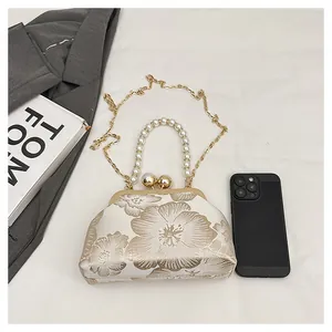 Detailed embroidery on shell bag with pearl handle and metal chain for size reference