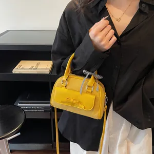 Bolso de ante amarillo con lazo y cinta de cuadros mostrado por una modelo con camisa