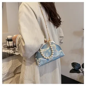 Detail of light blue shell bag with floral embroidery and pearl handle worn by model