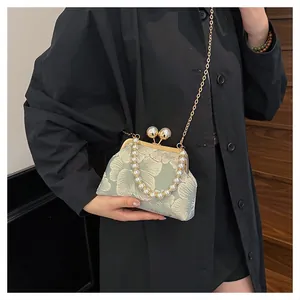 Detail of floral embroidery on a shell-shaped crossbody bag with pearl strap handle