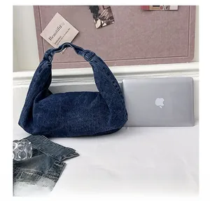 Blue denim hobo bag shown next to a laptop to demonstrate large storage capacity
