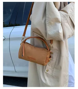 Detalle de un bolso bandolera cilíndrico marrón con textura mate y etiqueta de marca