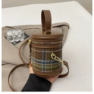 Detalle del patrón de cuadros retro y adornos de cuero marrón en un bolso de cubo cilindro